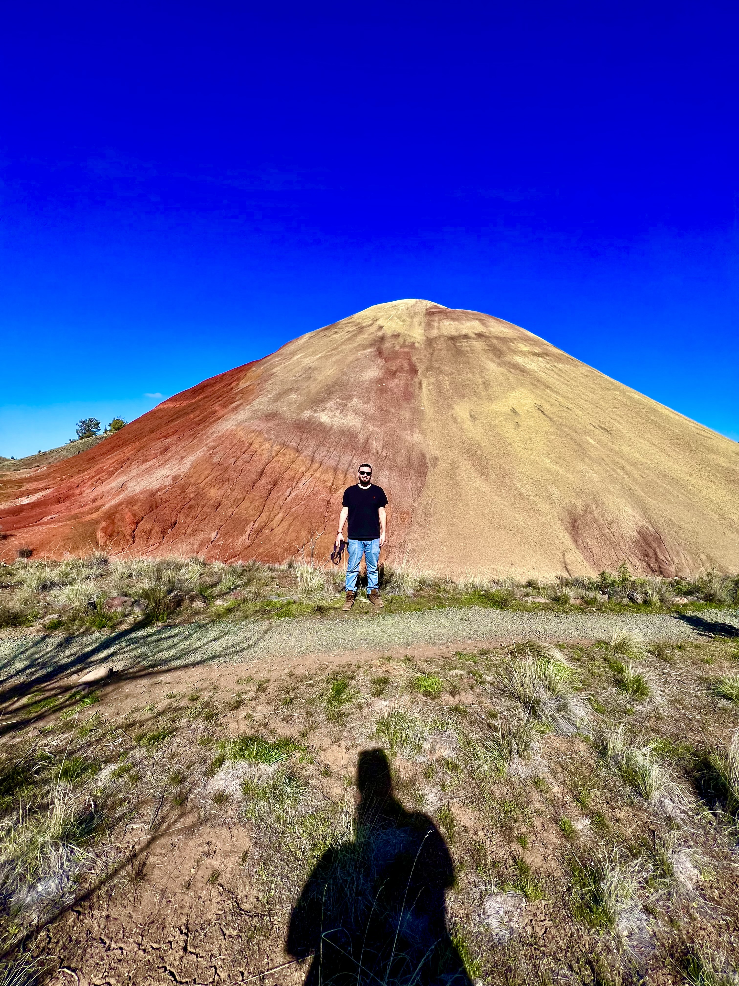 Hiker walking up the bright red and yellow cone-shaped knoll on the Red Hill Trail at the Painted Hills Unit