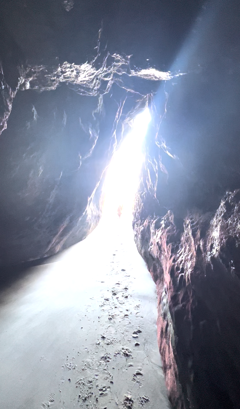 Light streaming into the second Hug Point sea cave with sand and rocks on the floor