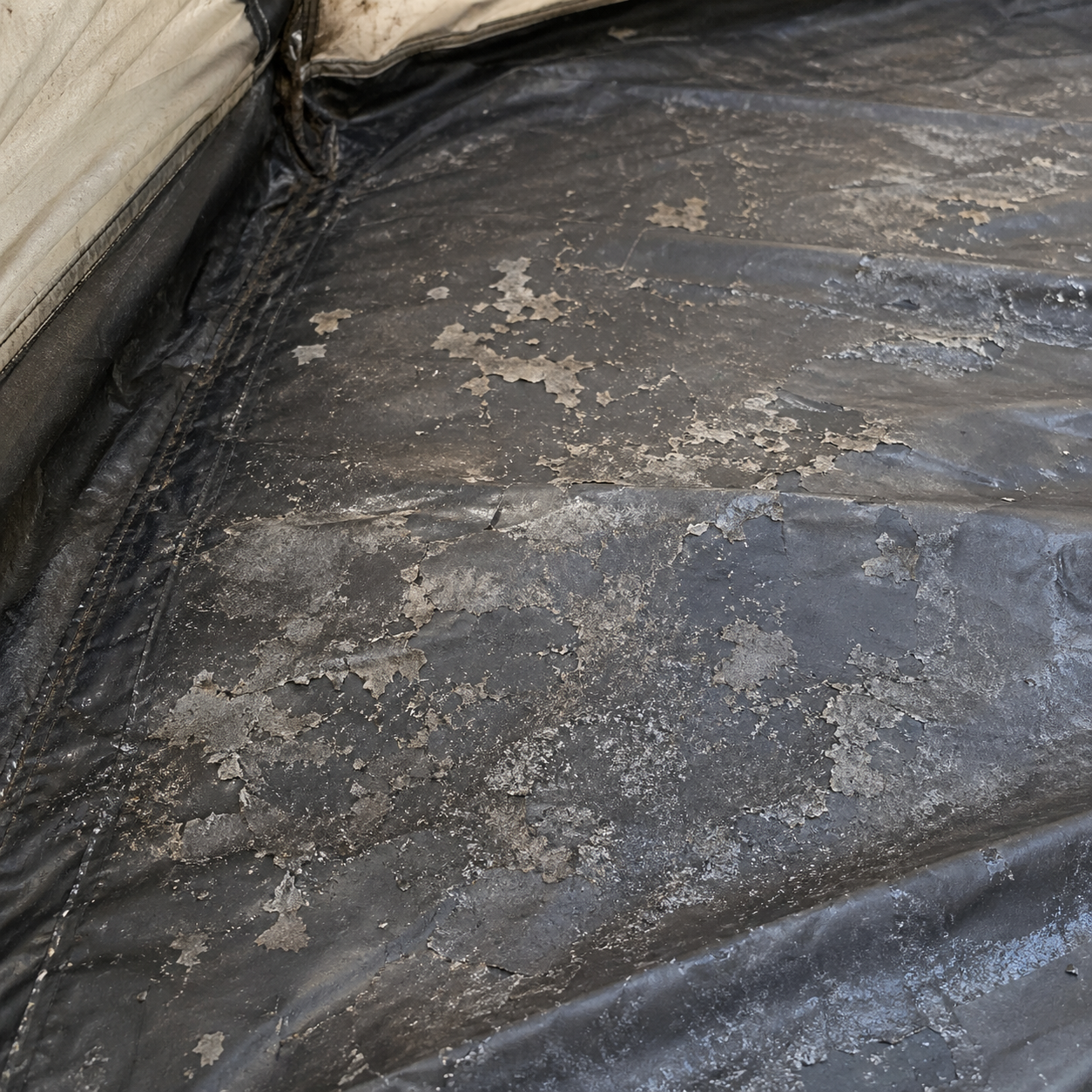 Macro close-up of a tent floor interior showing visible polyurethane coating failure: flaking, peeling pieces of clear coating lifting off the fabric and a discolored sticky area indicating hydrolysis