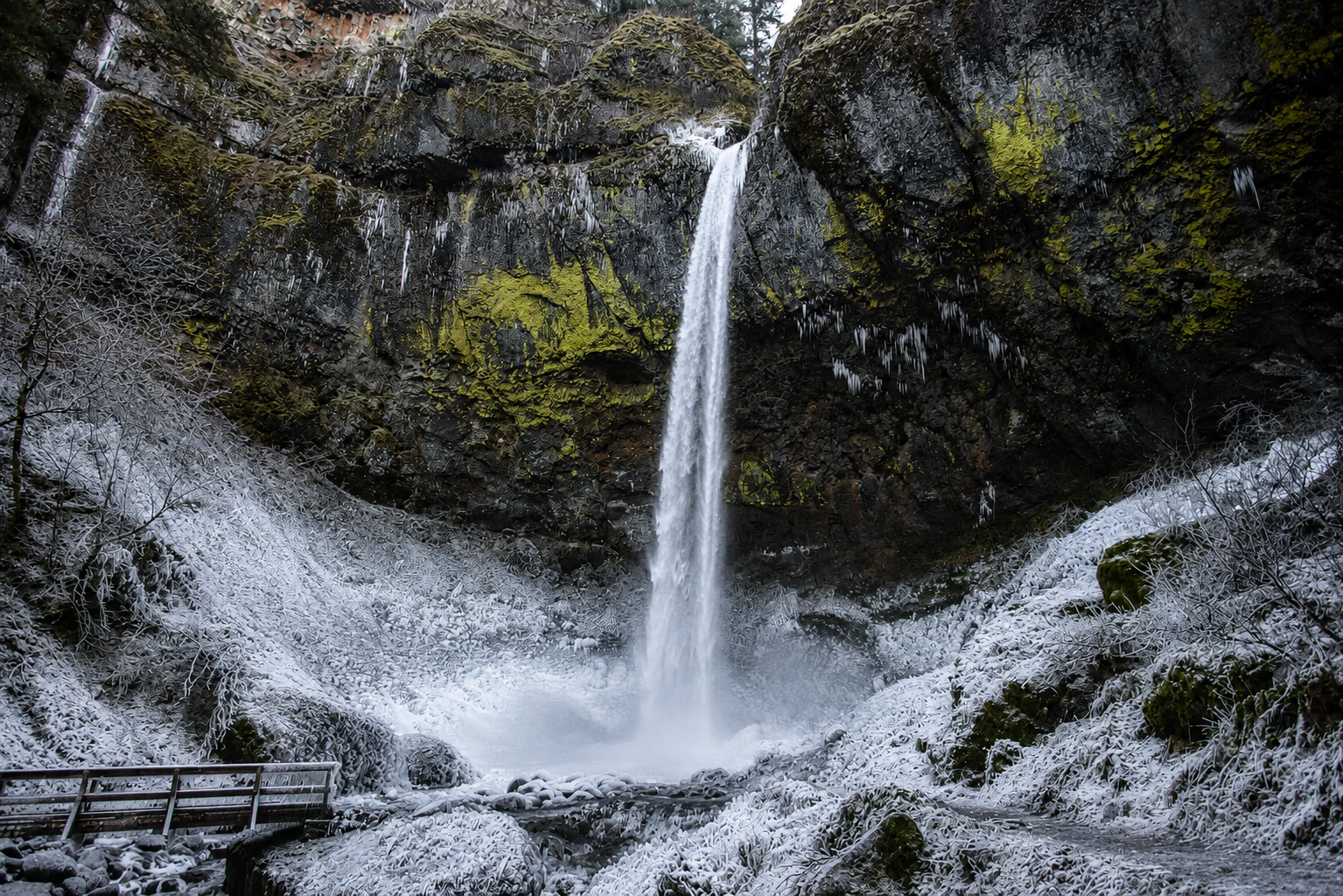 Elowah Falls in winter with snow-covered rocks and ice formations surrounding the frozen waterfall in the Columbia River Gorge Oregon